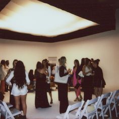 a group of people standing around each other in a room with white folding chairs on the floor