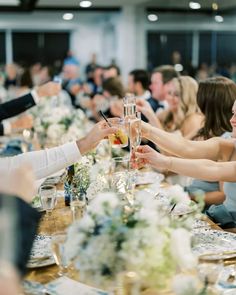 people sitting at a long table toasting each other's glasses with their hands