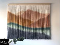 the wall hanging is made out of yarn and fringes, with a plant in front of it