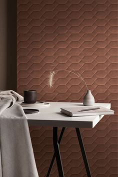 a white table topped with a vase next to a wall covered in brown geometric tiles