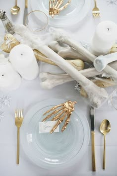 the table is set with gold and white dishes, silverware, candles and napkins