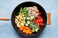 vegetables are being cooked in a skillet on a blue tablecloth with a wooden spatula