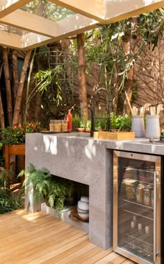 an outdoor kitchen with wood flooring and concrete counter tops, surrounded by plants and trees