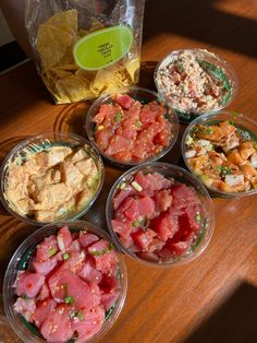 six bowls filled with different types of food on top of a wooden table next to a bag of chips