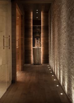 an empty hallway with lights on the walls and wood flooring is lit by recessed lighting