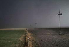 an empty field with power lines and telephone poles in the distance on a dark, overcast day