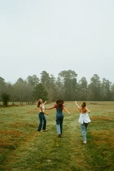 three girls are running in the grass with their arms around each other as they fly a kite