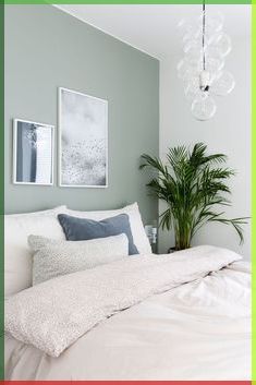 a bed with white sheets and pillows next to a potted plant