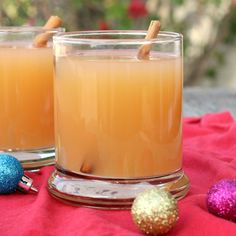 two glasses filled with orange juice sitting on top of a red cloth next to christmas ornaments