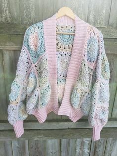 a crocheted sweater hanging up on a wooden fence with an open front cardigan