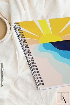 a spiral notebook sitting on top of a white table next to a cup of coffee