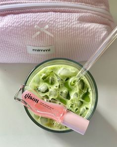 a pink and white bag sitting next to a green smoothie in a glass cup