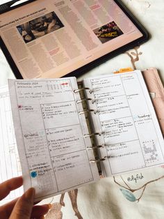 a person is holding an open planner in front of a tablet computer on a bed