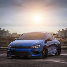 a blue car parked on the side of a road with the sun in the background