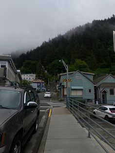 cars parked on the side of a road next to houses and mountains in the background