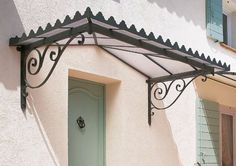 a white building with green doors and a black iron awning over the front door