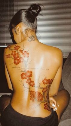 a woman sitting on top of a couch next to a window with flowers tattooed on her back