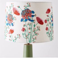 a lamp with flowers painted on it and a green metal base, sitting against a white wall