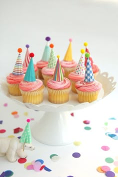 cupcakes with pink frosting and colorful party hats on a cake platter