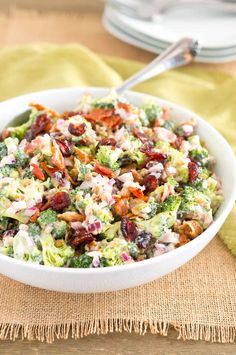 a white bowl filled with broccoli salad on top of a wooden table next to a green napkin