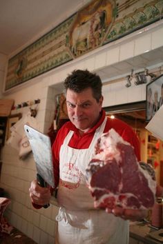 a man in an apron holding up some meat