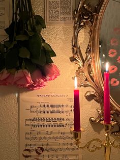 two candles are lit in front of a mirror with music sheets on the wall behind it