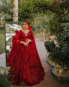 a woman wearing a red gown and veil in the middle of a courtyard with trees