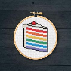 a cross stitch rainbow flag on a wooden wall hanging in front of a black background