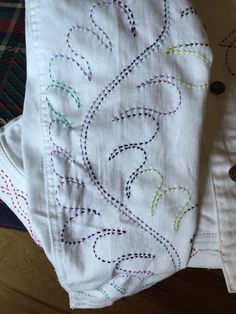 two white shirts with colorful designs on them sitting on top of a wooden floor next to a plaid table cloth