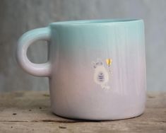 a white and blue coffee mug with a cat on it's side sitting on a wooden table