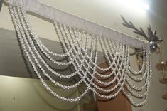 a curtain with beads hanging from it's side in front of a wall mounted mirror