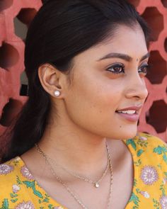 a woman wearing a yellow top and gold necklace with pearls on her left side, looking at the camera