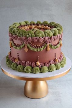 a three layer cake with green and pink icing on a gold plated stand