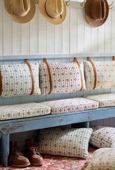 several hats are hanging on the wall above a bench with pillows and shoes underneath it