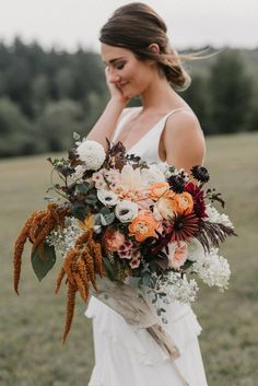 a woman in a white dress holding a large bouquet with orange and pink flowers on it