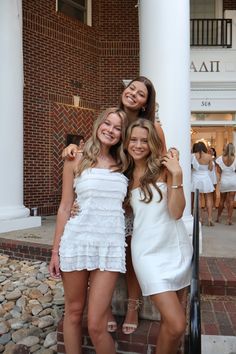 three beautiful young women standing next to each other in front of a building with white pillars