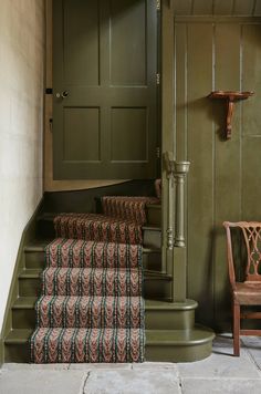 a green door and some stairs in a room with a chair on the floor next to it