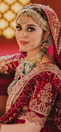 a woman wearing a red and gold bridal outfit with jewelry on her head, sitting in