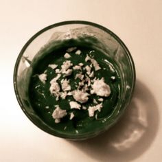 a green bowl filled with food sitting on top of a white table next to a spoon