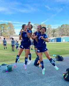 three girls are jumping in the air with their arms around each other on a soccer field