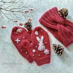 two red mittens with white snowflakes are next to pine cones and branches