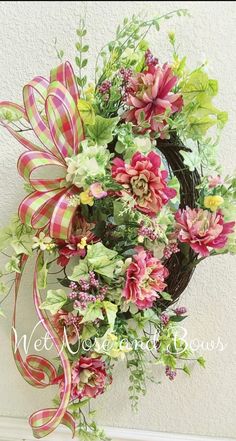 a wreath with pink and green flowers hanging on the wall next to a white door