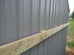 the side of a metal building with wood planks on it's sides and grass in the background