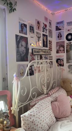 a white bed topped with lots of pillows next to a wall covered in pictures and posters