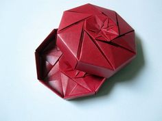 a red origami box sitting on top of a white table next to a piece of paper