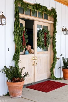 two potted plants are sitting on the front porch with christmas wreaths hanging over them