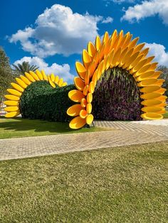 a large sunflower sculpture in the middle of a grassy area next to a hedge