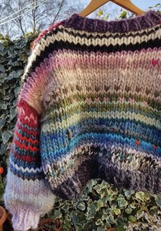 a multicolored sweater hanging on a wooden hanger in front of some plants