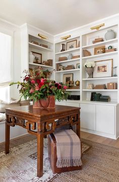 a vase with flowers on top of a wooden table in front of bookshelves