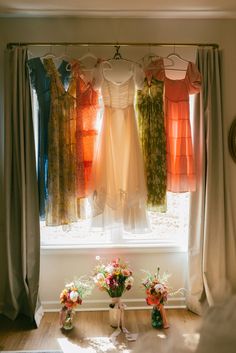 dresses hanging in front of a window with sun shining through the windowshade and flowers